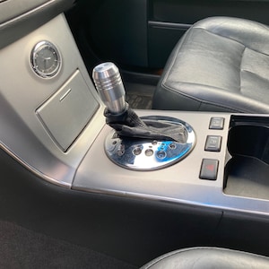 May include: Close-up of a silver car interior with a silver gear shift knob, a silver clock, and a silver and black centre console with buttons.