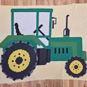 May include: A handmade crochet blanket featuring a green tractor design. The tractor has black tires with yellow centers, a white cab, and is set against a light yellow background. The blanket is made with a corner-to-corner crochet stitch.