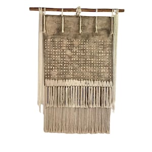 May include: A brown and white woven wall hanging with a fringe border. The hanging is made of natural fibers and has a geometric pattern.