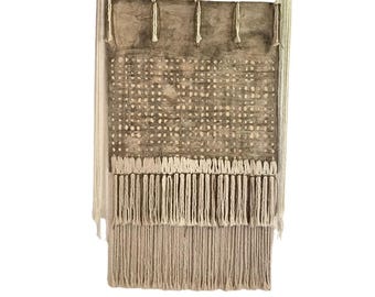 May include: A brown and white woven wall hanging with a fringe border. The hanging is made of natural fibers and has a geometric pattern.