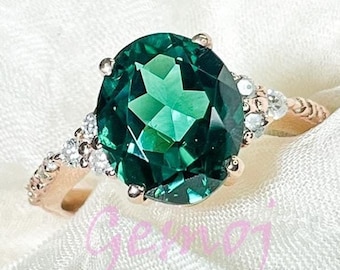 May include: A rose gold ring with a large oval-shaped green gemstone surrounded by smaller clear gemstones.