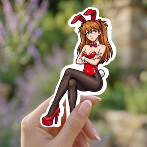 May include: A sticker featuring an anime-style character in a red bunny suit with matching ears and bow tie. The character is wearing black tights and red platform heels. The sticker is held in a hand.