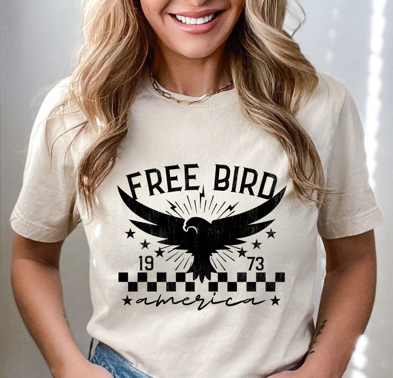 May include: A beige t-shirt with a black graphic of an eagle with the text "FREE BIRD" above it and "1973 america" below it.