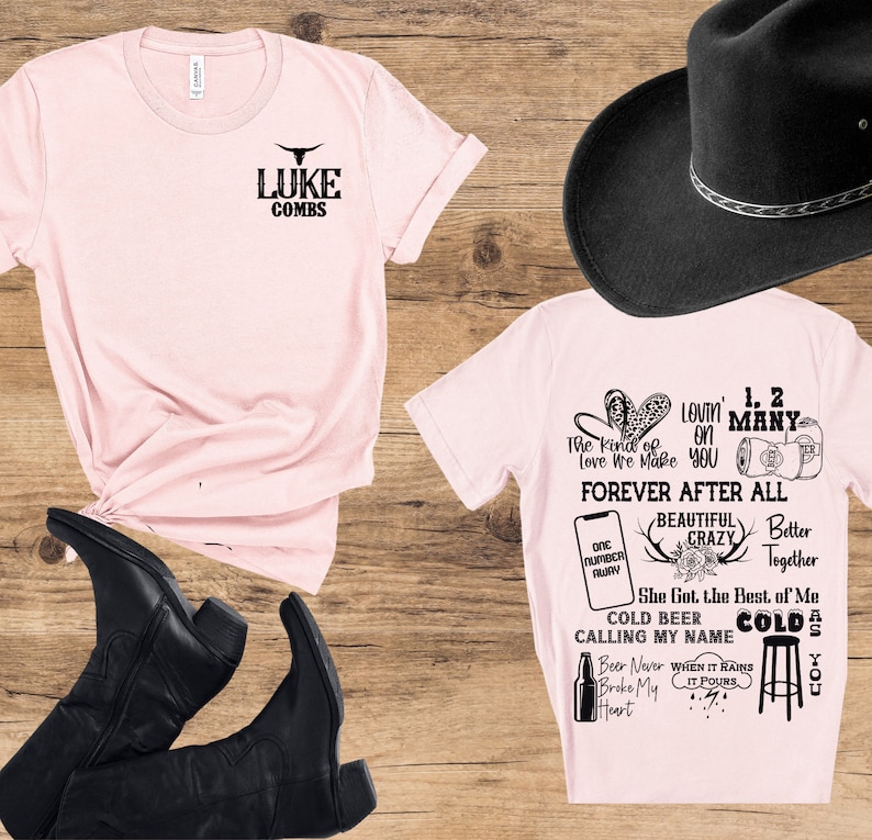 May include: A light pink t-shirt with the text "LUKE COMBS" and a bull graphic. A second light pink t-shirt features song lyrics and graphics. Black cowboy boots and a black cowboy hat are also in the image.