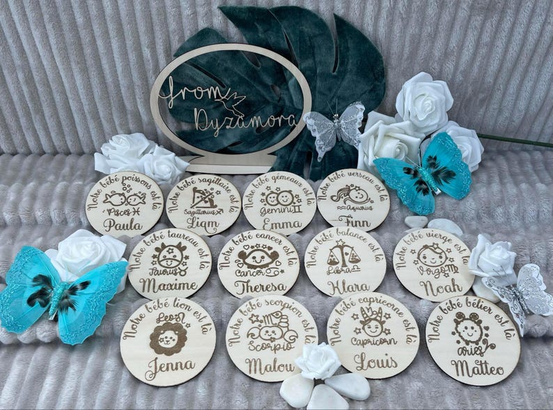May include: Twelve round wooden plaques with zodiac signs and names. The plaques are arranged in a circle with a white background. The zodiac signs are: Pisces, Sagittarius, Gemini, Aquarius, Taurus, Cancer, Libra, Virgo, Leo, Scorpio, Capricorn, and Aries. The names are: Paula, Liam, Emma, Finn, Maxime, Theresa, Klara, Noah, Jenna, Malou, Louis, and Matteo.