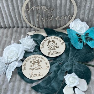 May include: Two wooden circular signs with a baby's name and zodiac sign. The first sign is brown with the text 'Notre bebe belier est la aries Matteo'. The second sign is brown with the text 'Notre bebe capricorne est la Capricorn Louis'. Both signs have a cartoon image of the zodiac sign.