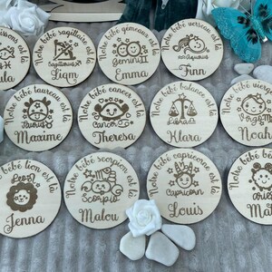 May include: Twelve round wooden plaques with engraved zodiac signs and names. Each plaque has a white background with brown engraved text and images. The plaques are arranged in a circle, with the names 'Paula', 'Liam', 'Emma', 'Finn', 'Maxime', 'Theresa', 'Klara', 'Noah', 'Jenna', 'Malou', 'Louis', and 'Matteo' visible.