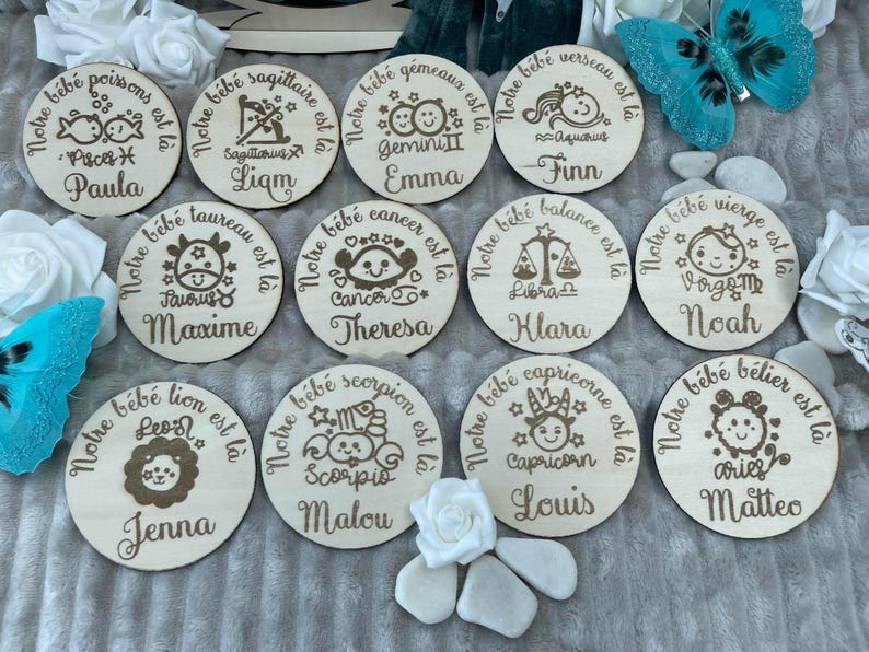 May include: Twelve round wooden plaques with engraved zodiac signs and names. Each plaque has a white background with brown engraved text and images. The plaques are arranged in a circle, with the names 'Paula', 'Liam', 'Emma', 'Finn', 'Maxime', 'Theresa', 'Klara', 'Noah', 'Jenna', 'Malou', 'Louis', and 'Matteo' visible.