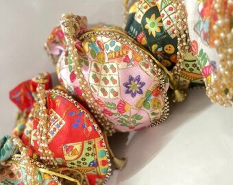 May include: A stack of four colorful drawstring bags with intricate patterns and gold trim. Each bag has a pearl and gold chain embellishment.