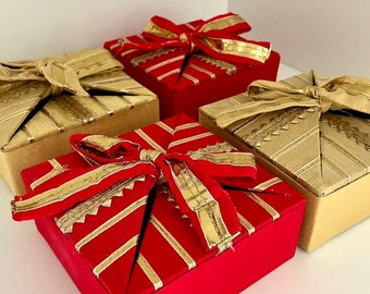 May include: Four gift boxes wrapped in gold and red paper with gold ribbon. The boxes are arranged in a pyramid shape.