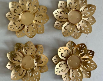 Könnte beinhalten: Vier goldene Kerzenhalter aus Metall mit filigranen Ausschnitten. Jeder Halter hat eine kreisförmige Öffnung in der Mitte für ein Teelicht.