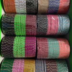 May include: A set of colorful bangles with gold accents. The bangles are stacked in rows and are made of a variety of materials, including glass, metal, and plastic.