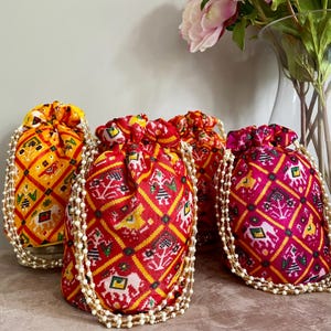 May include: Four colourful drawstring bags with pearl trim. The bags are made of fabric with a geometric pattern and are in shades of yellow, red, pink, and green.