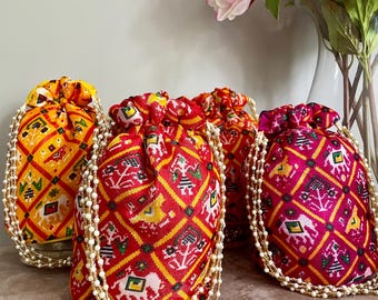 Puede incluir: Cuatro bolsas de cordón de colores con ribete de perlas. Las bolsas están hechas de tela con un patrón geométrico y son en tonos amarillo, rojo, rosa y verde.