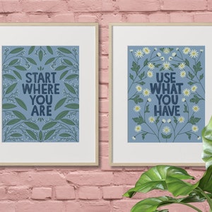 Può includere: Due stampe incorniciate con sfondi blu e motivi floreali bianchi. La stampa a sinistra dice "Start Where You Are" e la stampa a destra dice "Use What You Have".