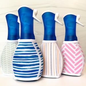 May include: Four spray bottles with blue plastic nozzles and white trigger mechanisms. Each bottle is encased in a fabric sleeve featuring distinct patterns: a gray herringbone, blue horizontal stripes, orange vertical stripes, and pink diagonal lines.