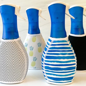 May include: Four blue spray bottles with different patterned covers. The covers are black, white with blue stripes, white with pineapple designs, and white with black chevron patterns.