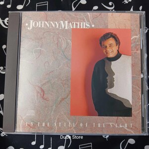 May include: A CD case featuring Johnny Mathis' album "In the Still of the Night." The cover art includes a portrait of Mathis in a black and white sweater with a silhouette design. The CD case is in a clear plastic case.