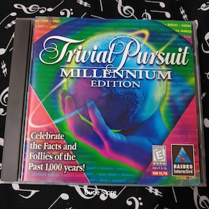 Peut inclure: Jeu Trivial Pursuit Millennium Edition sur CD-ROM. La boîte du jeu présente un design coloré avec un globe et une main. Le texte indique "Célébrez les faits et les folies des 1 000 dernières années !" et comprend la classification ESRB.