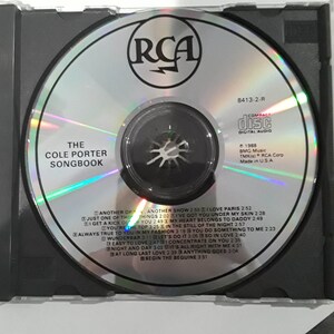 May include: A silver compact disc with a rainbow holographic effect. The disc features the RCA logo, the title "The Cole Porter Songbook", and a list of songs including "Another Op'nin', Another Show", "I Love Paris", "Just One of Those Things", "I've Got You Under My Skin", "My Heart Belongs to Daddy", "You're the Top", "In the Still of the Night", "Always True to You in My Fashion", "You Do Something to Me", "Wunderbar", "Let's Do It", "So in Love", "Easy to Love", "Concentrate on You", "Night and Day", "It's All Right with Me", "At Long Last Love", "Anything Goes", and "Begin the Beguine".