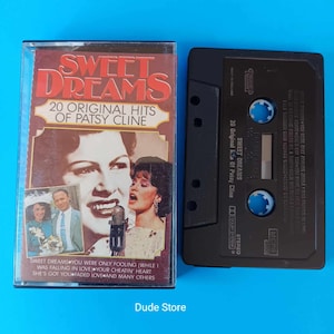 May include: A vintage cassette tape of Patsy Cline's "Sweet Dreams: 20 Original Hits." The album cover features a portrait of Cline and the album title in red. The black cassette tape is next to the case on a blue surface.