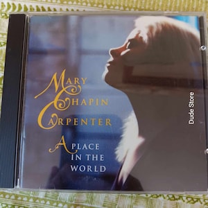 May include: A CD case featuring a photograph of a woman looking upwards. The album title is "Mary Chapin Carpenter: A Place in the World".