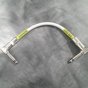 Puede incluir: Cable de instrumento blanco con conectores en ángulo recto en ambos extremos. El cable está etiquetado con "ERNIE BALL" e "INSTRUMENT" en letras amarillas.