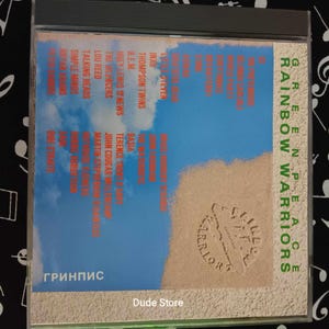 Puede incluir: Una caja de CD con un fondo azul y blanco que presenta una escena de playa. El texto "GREENPEACE RAINBOW WARRIORS" está impreso en rojo en la caja. La parte posterior de la caja enumera varios artistas, incluidos INXS, Thompson Twins, R.E.M., Huey Lewis and the News, The Lencers, Lou Reed, Talking Heads, Simple Minds, Bryan Adams, Basia, Terence Trent D'Arby, John Cougar Mellencamp, Martin Stephenson, y más. El texto "ГРИНПИС" está impreso en rojo en la parte inferior de la caja.