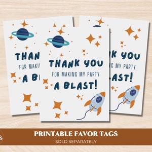 May include: Three printable favor tags with a space theme. The tags are white with blue and orange accents. The text on the tags reads "Thank you for making my party a blast!"  The tags are perfect for a space-themed party.
