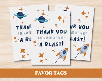Pode incluir: Três etiquetas de lembrancinhas brancas com tema espacial. Cada etiqueta apresenta um planeta azul com anéis, estrelas laranja e um foguete. O texto diz "Thank You for Making My Party a Blast!" e "Favor Tags".