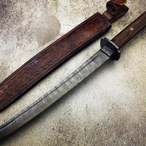 May include: A handcrafted Damascus steel knife with a wooden handle and a brown leather sheath. The blade has a unique pattern, and the sheath is embossed with a decorative design. The knife is a handmade item.
