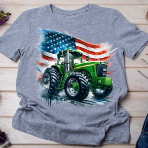 K&ouml;nnte beinhalten: Ein graues T-Shirt mit einem gr&uuml;nen Traktor, der vor einer amerikanischen Flagge f&auml;hrt. Der Traktor hat gro&szlig;e Reifen und eine gr&uuml;ne Kabine.