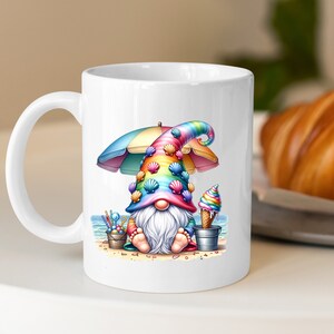May include: White ceramic coffee mug featuring a colourful gnome illustration. The gnome is wearing a rainbow hat with seashells and holding an ice cream cone. The gnome is sitting on a beach under a colourful umbrella.