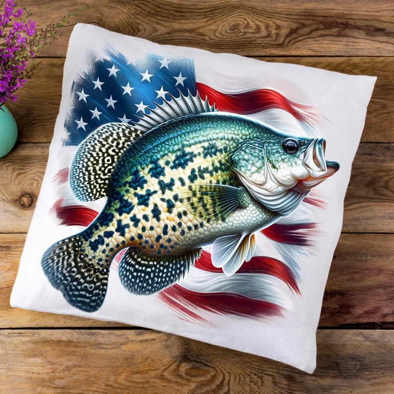 Op de afbeelding: Een wit kussen met een kleurrijk beeld van een vis met zwarte vlekken op een rood-wit-blauwe Amerikaanse vlag achtergrond.
