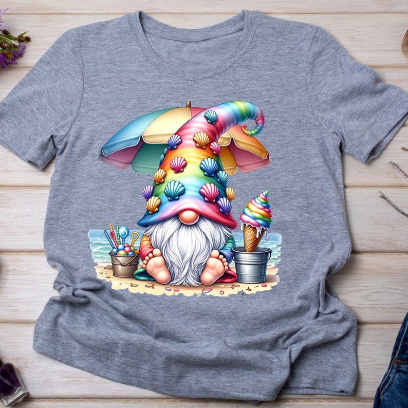 May include: A grey t-shirt featuring a colourful gnome wearing a rainbow hat with seashells, holding an ice cream cone and sitting under a beach umbrella. The gnome is on a beach with a bucket and spade.