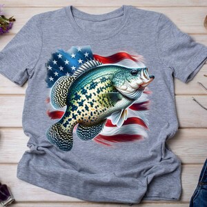 Op de afbeelding: Een grijs T-shirt met een afbeelding van een baars die uit het water springt voor een Amerikaanse vlag.