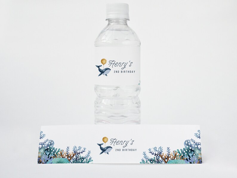 May include: Water bottle label featuring a blue whale holding a gold balloon. The label reads "Henry's 2nd Birthday". A matching banner with a whale and coral reef design is also included.