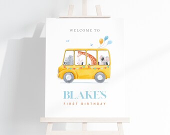 May include: A yellow school bus with a giraffe, hippopotamus, rabbit, and koala riding inside. The bus has colorful flags and balloons. The text "WELCOME TO BLAKE'S FIRST BIRTHDAY" is printed on the sign.