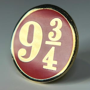 May include: A gold-colored pin with a red background and the numbers "9 3/4" in gold.