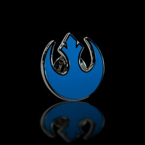 May include: A blue and silver Rebel Alliance symbol pin. The pin is a popular symbol from the Star Wars franchise.