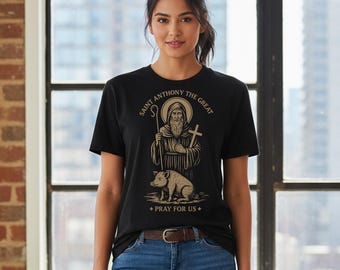 May include: Black t-shirt featuring a graphic of Saint Anthony the Great with a pig and the text "Saint Anthony the Great + Pray for Us +". The shirt is worn by a person in blue jeans.