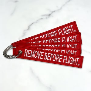 May include: A set of six red keychains with white embroidered text that reads "REMOVE BEFORE FLIGHT".