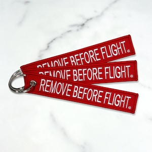 May include: Three red fabric keychains with white embroidered text that reads "REMOVE BEFORE FLIGHT".