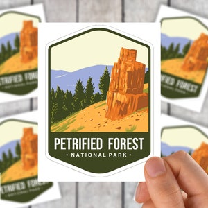May include: A collection of stickers featuring a landscape design for Petrified Forest National Park. The design includes a rock formation, trees, and the park's name. The stickers are white with a green, tan, and blue color scheme.