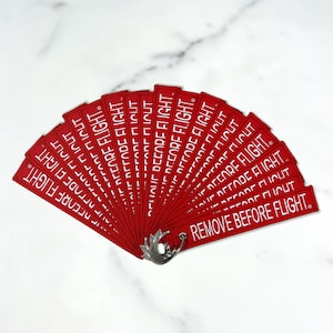 May include: A fan of red fabric keychains with the text "REMOVE BEFORE FLIGHT" printed in white.