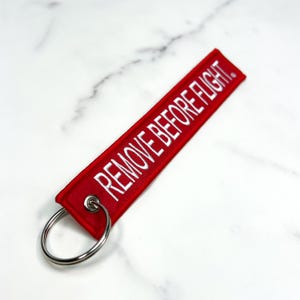 May include: Red keychain with a white embroidered label that says "REMOVE BEFORE FLIGHT".