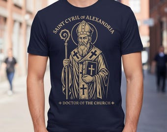 May include: Navy blue t-shirt featuring a detailed illustration of Saint Cyril of Alexandria, holding a staff and book. The text above reads "Saint Cyril of Alexandria" and below "Doctor of the Church" in a gold color.