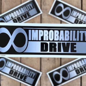 May include: A silver and black sticker with the text "IMPROBABILITY DRIVE" and an infinity symbol. The sticker is on a wooden background.