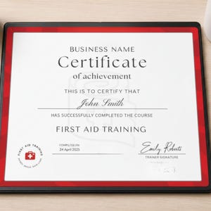 Può includere: Certificato incorniciato con bordo rosso, che mostra il testo "Certificate of achievement" e "First Aid Training". Il certificato è assegnato a "John Smith" e datato 24 aprile 2025. La cornice è nera.