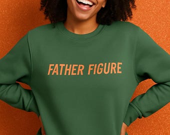 May include: A green sweatshirt with the text "FATHER FIGURE" in orange. The person wearing the sweatshirt is smiling in front of an orange background. The sweatshirt is a solid color and has a crew neck.